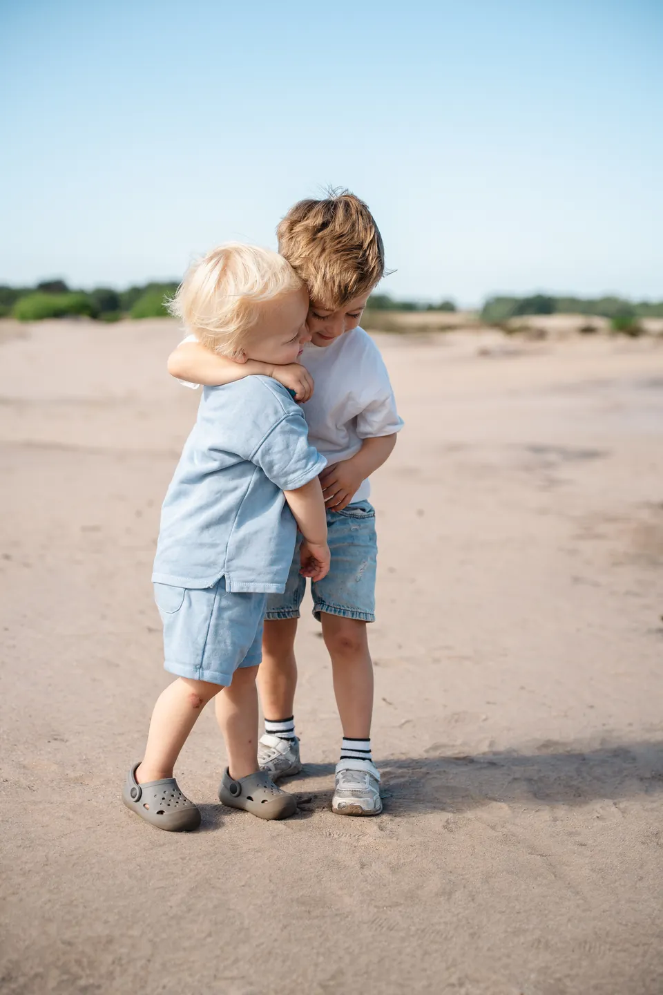 Twee broertjes knuffelen elkaar op een zandvlakte