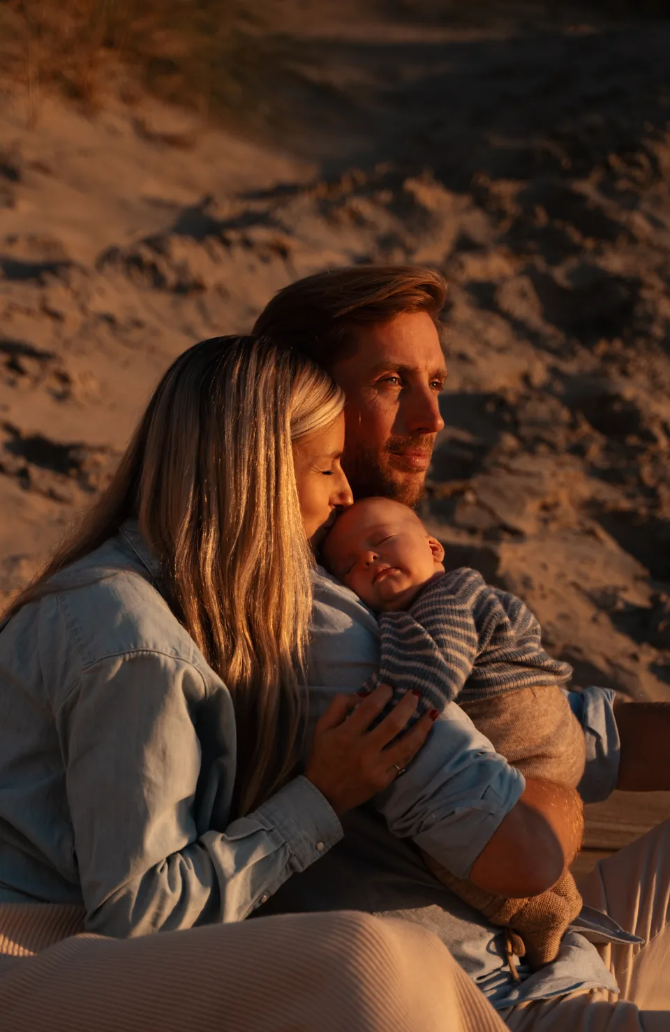 Ouders met hun slapende baby in de duinen bij zonsondergang
